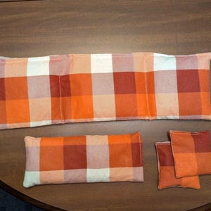 May include: Four orange and white plaid fabric heat packs. The largest pack is rectangular and divided into three sections. The other three packs are smaller and square.