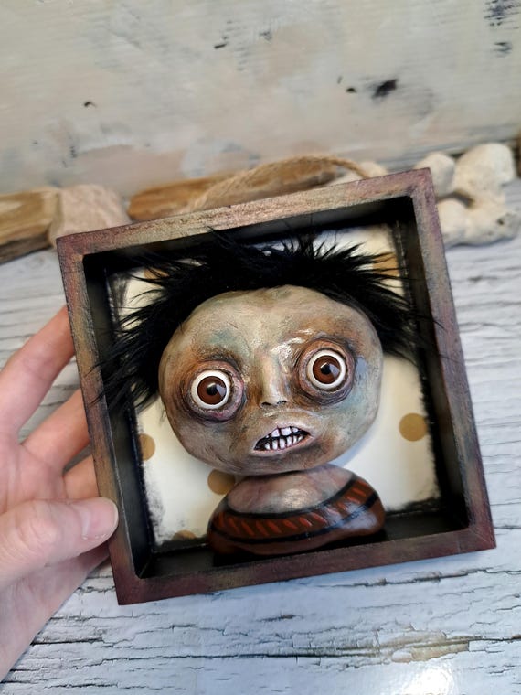 A one-of-a-kind handmade clay face shadowbox that sits somewhere between curiosity cabinet artifact and fever dream — the kind of thing that makes guests stop mid-sentence.