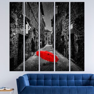 May include: A black and white photograph of a narrow alleyway in a city. The alleyway is lined with brick buildings and there is a red umbrella lying in the middle of the street.