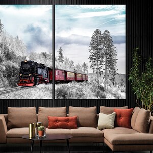 May include: A two-panel canvas print depicting a vintage steam train traveling through a snowy forest. The train is black and red, with several red passenger cars. The forest is in black and white, with a blue sky in the background.