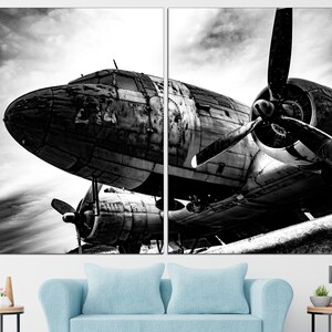 May include: A black and white photograph of a vintage airplane with a propeller. The airplane is sitting on the ground with the propeller facing the camera. The airplane is weathered and has a lot of detail.