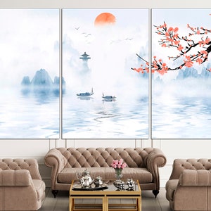 May include: A three-panel canvas print depicting a serene landscape with mountains, a lake, and a red sun. The mountains are painted in shades of blue and white, and the lake is a light blue with reflections of the mountains. The sun is a bright red circle in the sky. The print is framed in a white frame and is hanging on a white wall.
