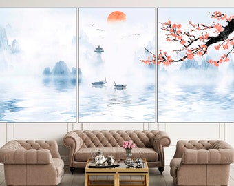 May include: A three-panel canvas print depicting a serene landscape with mountains, a lake, and a red sun. The mountains are painted in shades of blue and white, and the lake is a light blue with reflections of the mountains. The sun is a bright red circle in the sky. The print is framed in a white frame and is hanging on a white wall.