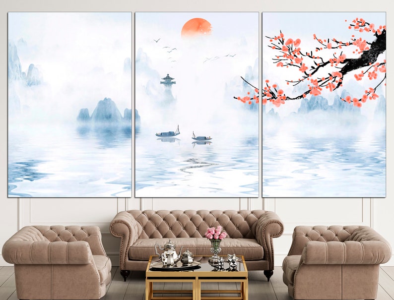 May include: A three-panel canvas print depicting a serene landscape with mountains, a lake, and a red sun. The mountains are painted in shades of blue and white, and the lake is a light blue with reflections of the mountains. The sun is a bright red circle in the sky. The print is framed in a white frame and is hanging on a white wall.