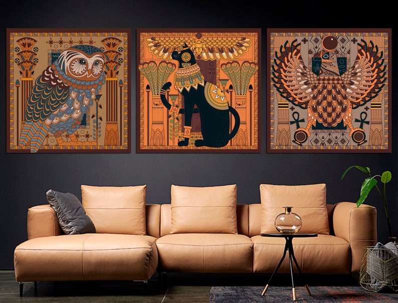May include: Three framed prints with an Egyptian theme. The first print features an owl with intricate details, the second print features a cat with wings, and the third print features a winged creature with a crown.
