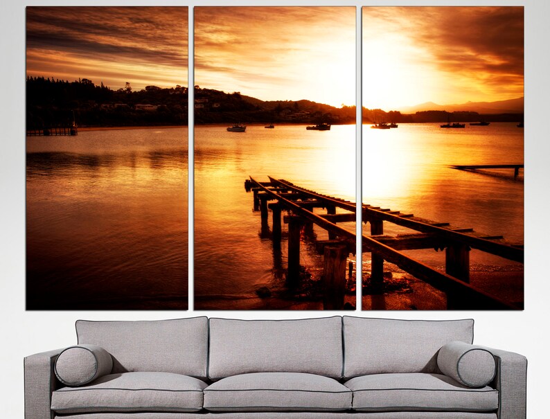 May include: A sunset over a body of water with a wooden pier extending into the water. The sky is a vibrant orange and yellow, and the water is a calm, reflective orange.