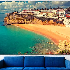 May include: A scenic view of a white-washed village perched on a cliff overlooking a turquoise bay with a sandy beach. The sky is a mix of blue and white clouds.