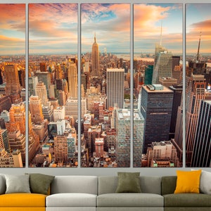 May include: A panoramic view of the New York City skyline at sunset. The image shows a dense collection of skyscrapers with a golden glow from the setting sun. The Empire State Building is visible in the center of the image.