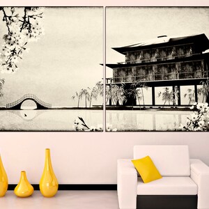 May include: A black and white print of a traditional Japanese house with a bridge and cherry blossoms. The print is framed and hanging on a white wall above a white sofa with a yellow pillow.