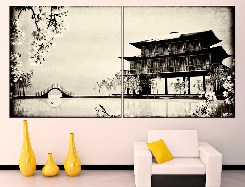 May include: A black and white print of a traditional Japanese house with a bridge and cherry blossoms. The print is framed and hanging on a white wall above a white sofa with a yellow pillow.