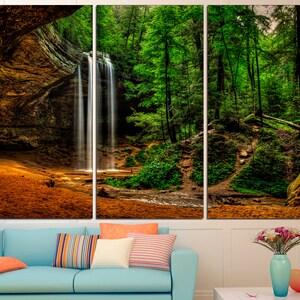 Peut inclure: Impression sur toile en trois panneaux repr&eacute;sentant une cascade se jetant dans un ruisseau, entour&eacute;e d'arbres verts luxuriants et d'une falaise rocheuse. L'&oelig;uvre pr&eacute;sente des tons chauds et terreux.