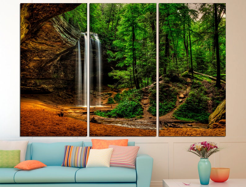 Peut inclure: Impression sur toile en trois panneaux repr&eacute;sentant une cascade se jetant dans un ruisseau, entour&eacute;e d'arbres verts luxuriants et d'une falaise rocheuse. L'&oelig;uvre pr&eacute;sente des tons chauds et terreux.