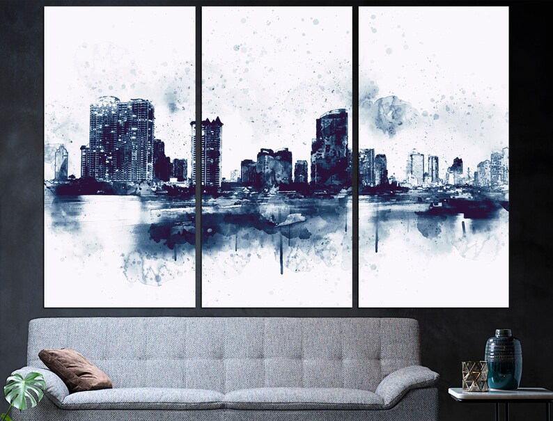 May include: A watercolor painting of a city skyline in shades of blue and white. The cityscape is reflected in the water below. The painting is divided into three panels.