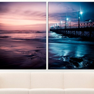 May include: Two-panel canvas art featuring coastal scenes. The left panel depicts a beach at sunset with pink and purple hues. The right panel shows a pier at night, illuminated by streetlights, with dark blue and teal tones.
