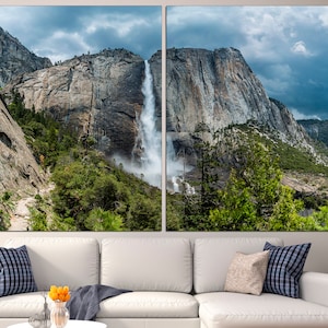 May include: A panoramic view of a waterfall cascading down a rocky cliff face in Yosemite National Park. Lush green trees and a cloudy sky complete the scene.