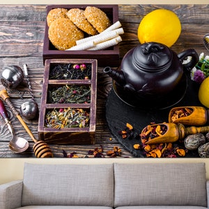 May include: A black teapot with a lid and a handle, sitting on a wooden table with a variety of loose leaf teas, tea infusers, lemons, and cookies.