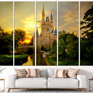 May include: A multi-panel canvas print depicting a fairytale castle with a moat and lush greenery, bathed in the golden light of a sunset. The castle is a light beige colour with blue accents and towers. The sky is a vibrant orange and yellow with fluffy clouds.
