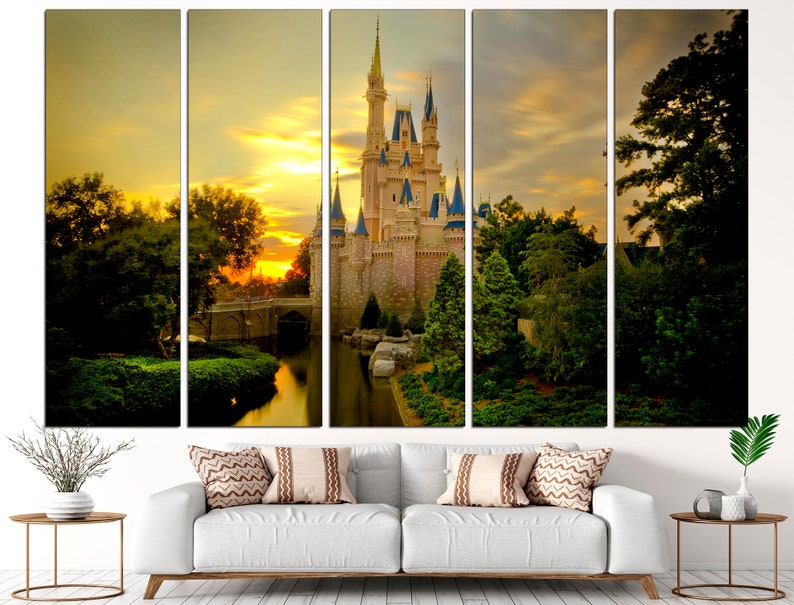 May include: A multi-panel canvas print depicting a fairytale castle with a moat and lush greenery, bathed in the golden light of a sunset. The castle is a light beige colour with blue accents and towers. The sky is a vibrant orange and yellow with fluffy clouds.