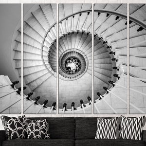 May include: A black and white photograph of a spiral staircase with a white railing. The staircase is made of stone and the railing is made of metal. The photo is taken from a low angle, looking up at the staircase.