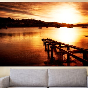 May include: A wooden pier extends into a calm body of water at sunset. The sky is a vibrant orange and yellow, with the sun setting in the distance. The water reflects the colors of the sky, creating a beautiful and serene scene.