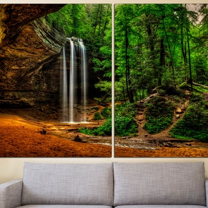 Peut inclure: Impression sur toile en deux panneaux repr&eacute;sentant une cascade se d&eacute;versant dans un plan d'eau. La cascade est entour&eacute;e d'arbres verts luxuriants et d'une falaise rocheuse. Le premier plan pr&eacute;sente une zone sablonneuse.