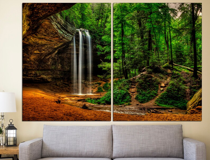 Peut inclure: Impression sur toile en deux panneaux repr&eacute;sentant une cascade se d&eacute;versant dans un plan d'eau. La cascade est entour&eacute;e d'arbres verts luxuriants et d'une falaise rocheuse. Le premier plan pr&eacute;sente une zone sablonneuse.