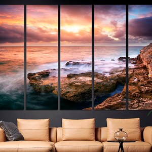 Pode incluir: Uma impress&atilde;o em tela de v&aacute;rios pain&eacute;is que representa uma paisagem costeira pitoresca ao p&ocirc;r do sol. A imagem apresenta uma costa rochosa com ondas quebrando e um c&eacute;u vibrante com tons de rosa, laranja e roxo.