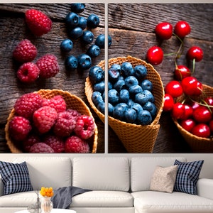 May include: A rustic wooden background with three waffle cones filled with blueberries, raspberries, and cherries. The cones are arranged in a row, with the blueberries in the center, the raspberries on the left, and the cherries on the right.