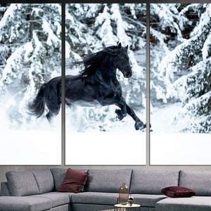 Op de afbeelding: Een zwart paard rent door een besneeuwd bos. Het paard is in beweging, met zijn manen en staart die in de wind wapperen. De sneeuw valt rond het paard en cre&euml;ert een prachtig winters tafereel.