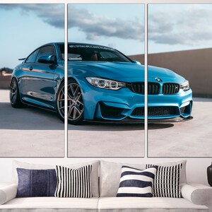 May include: A blue BMW M4 sports car parked on a concrete surface. The car has black wheels and a black front spoiler.