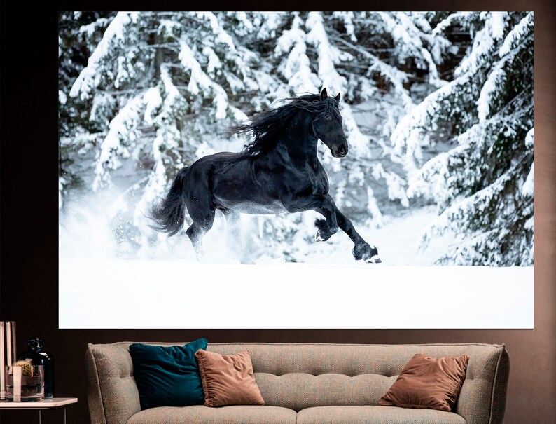 Op de afbeelding: Een zwart paard rent door een besneeuwd bos. Het paard is in beweging, met zijn manen en staart die in de wind wapperen. De met sneeuw bedekte bomen cre&euml;ren een winters decor.
