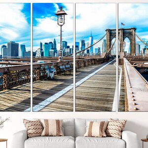 May include: A panoramic view of the Brooklyn Bridge in New York City. The bridge is a suspension bridge with a wooden walkway and a view of the city skyline in the background. The sky is blue with white clouds.