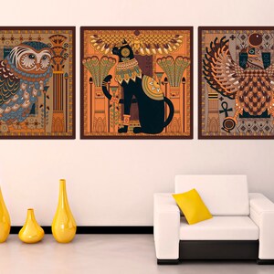 May include: Three framed prints with an Egyptian theme. The left print features a blue and brown owl with intricate details. The center print features a black cat with a gold collar and a crown. The right print features a brown and gold bird with a crown and an ankh.