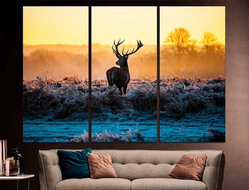 May include: A silhouette of a red deer stag with large antlers standing in a field of frosty grass at sunrise. The background is a hazy orange and yellow.
