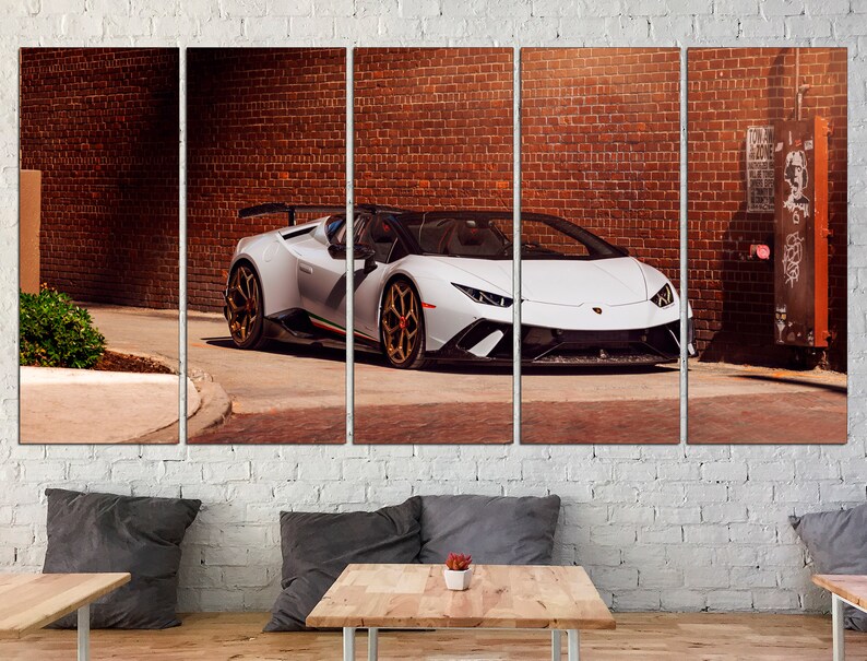 May include: A white Lamborghini Aventador SVJ Roadster parked in an alleyway with a brick wall in the background. The car has a black interior and gold wheels.