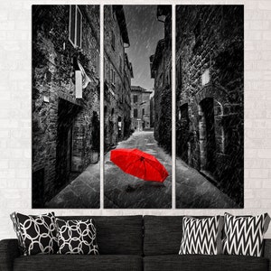 May include: A black and white photograph of a narrow street in a European city. The street is lined with old buildings and cobblestone. A red umbrella lies in the middle of the street.