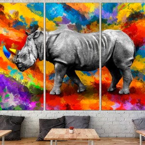May include: A black and white rhinoceros with a blue and yellow horn stands on a colorful abstract background. The background is a mix of orange, yellow, red, purple, blue, and green.