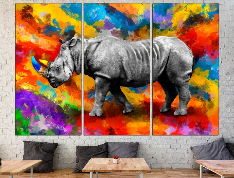 May include: A black and white rhinoceros with a blue and yellow horn stands on a colorful abstract background. The background is a mix of orange, yellow, red, purple, blue, and green.