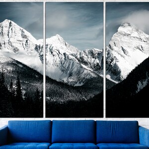 Puede incluir: Una vista panor&aacute;mica de monta&ntilde;as cubiertas de nieve con un bosque oscuro en primer plano. Las monta&ntilde;as est&aacute;n cubiertas de nieve blanca y el cielo es azul claro con algunas nubes.