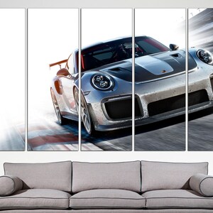 May include: A silver grey Porsche 911 GT2 RS sports car speeding on a race track. The car has a black stripe down the center of the hood and a black spoiler.