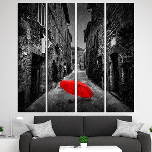 May include: A black and white photograph of a narrow street in a European city. The street is lined with old buildings and there is a red umbrella lying on the ground in the middle of the street.