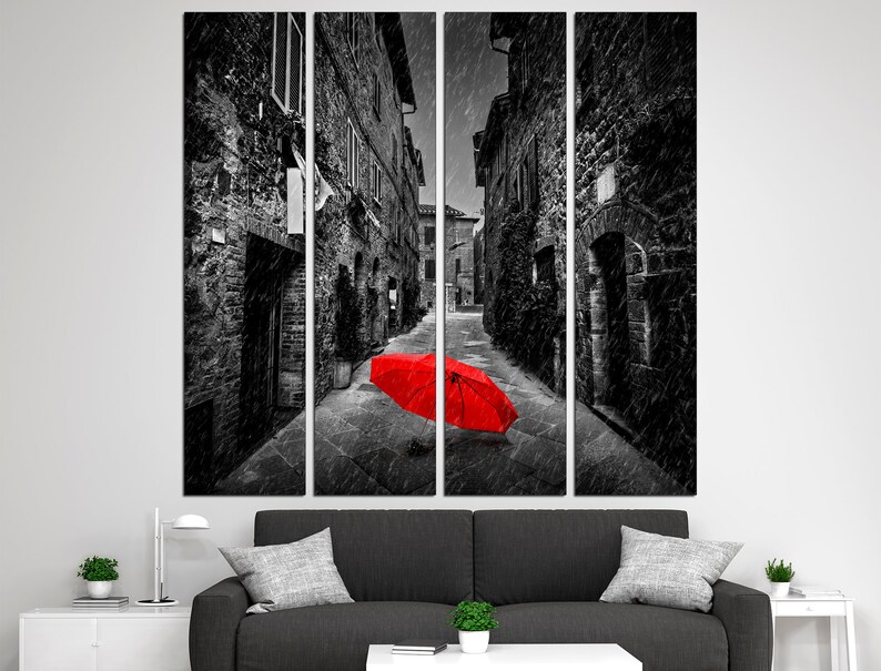 May include: A black and white photograph of a narrow street in a European city. The street is lined with old buildings and there is a red umbrella lying on the ground in the middle of the street.