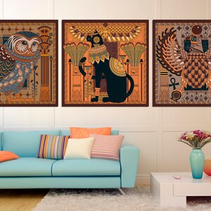 May include: Three framed prints with an Egyptian theme. The first print features a blue and green owl with a brown background. The second print features a black cat with a gold crown and a brown background. The third print features a brown and gold winged creature with a brown background.