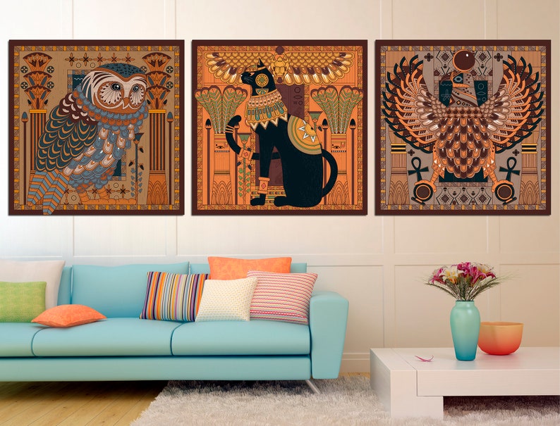 May include: Three framed prints with an Egyptian theme. The first print features a blue and green owl with a brown background. The second print features a black cat with a gold crown and a brown background. The third print features a brown and gold winged creature with a brown background.