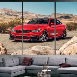 May include: A red BMW M4 sports car with black accents and black wheels is parked on a dirt road in a desert landscape. The car has a "Forged" sticker on the side.
