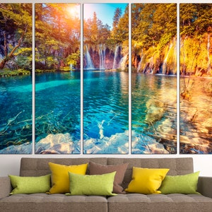 May include: A multi-panel canvas print featuring a scenic waterfall cascading into a turquoise lake surrounded by lush green and yellow trees. The image is split into five panels, creating a panoramic view of the natural landscape.