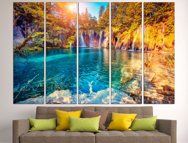 May include: A multi-panel canvas print featuring a scenic waterfall cascading into a turquoise lake surrounded by lush green and yellow trees. The image is split into five panels, creating a panoramic view of the natural landscape.