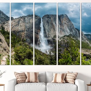 May include: A panoramic view of a waterfall cascading down a rocky cliff face in Yosemite National Park. Lush green trees and a cloudy sky complete the scene.