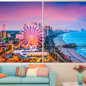 May include: A panoramic view of Myrtle Beach, South Carolina at sunset. The Ferris wheel is lit up in pink and white, and the beach is lined with palm trees and buildings. The ocean is a vibrant blue, and the sky is a mix of pink, purple, and orange.