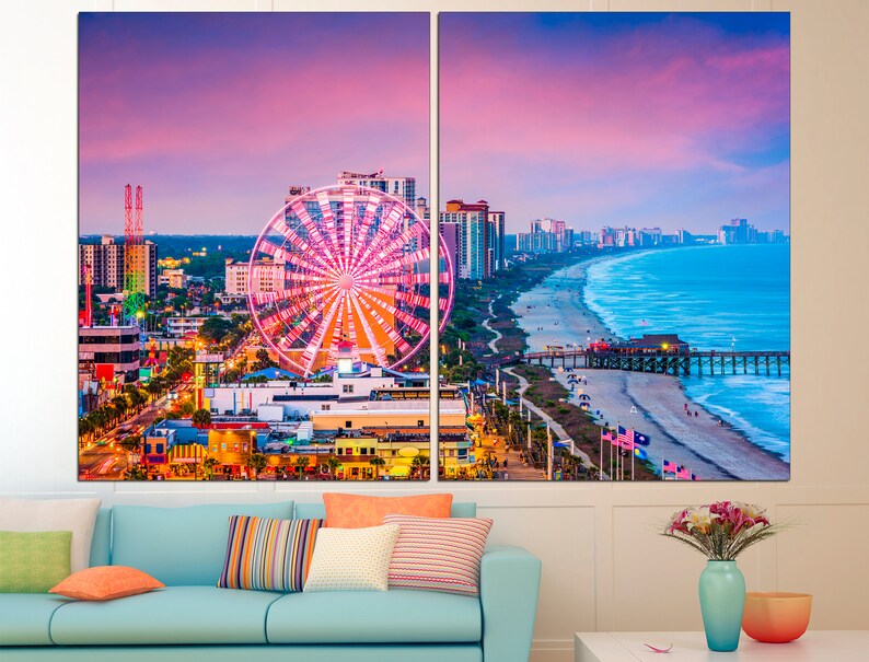 May include: A panoramic view of Myrtle Beach, South Carolina at sunset. The Ferris wheel is lit up in pink and white, and the beach is lined with palm trees and buildings. The ocean is a vibrant blue, and the sky is a mix of pink, purple, and orange.